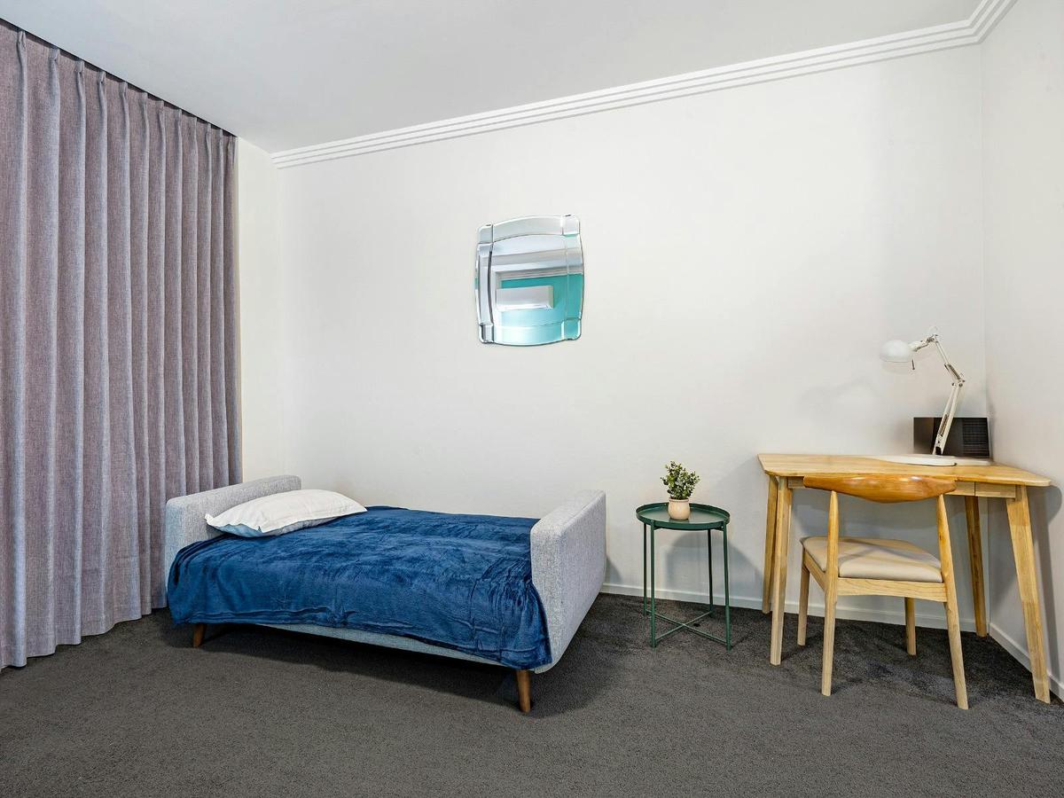 Studio room featuring a sofa bed, bedside table, work desk, and floor-to-ceiling curtains.