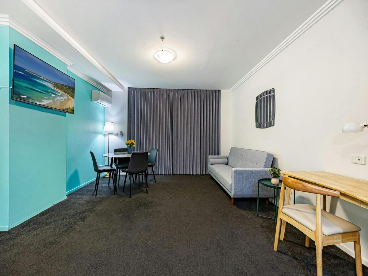 Spacious open-plan studio with sofa bed, dining table, and teal feature wall.
