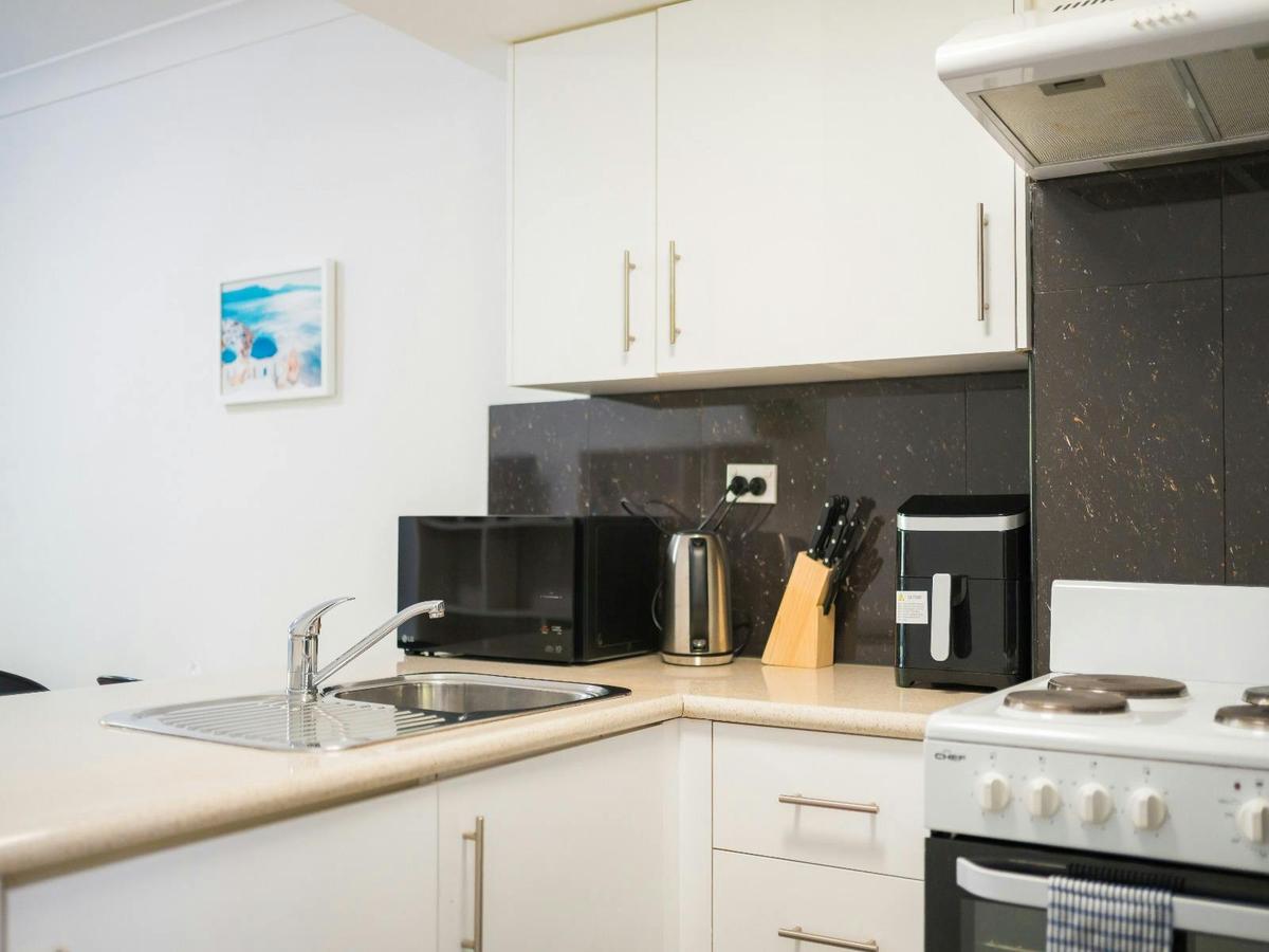 Modern kitchen with white cabinetry, cooktop, oven, microwave and breakfast bench.