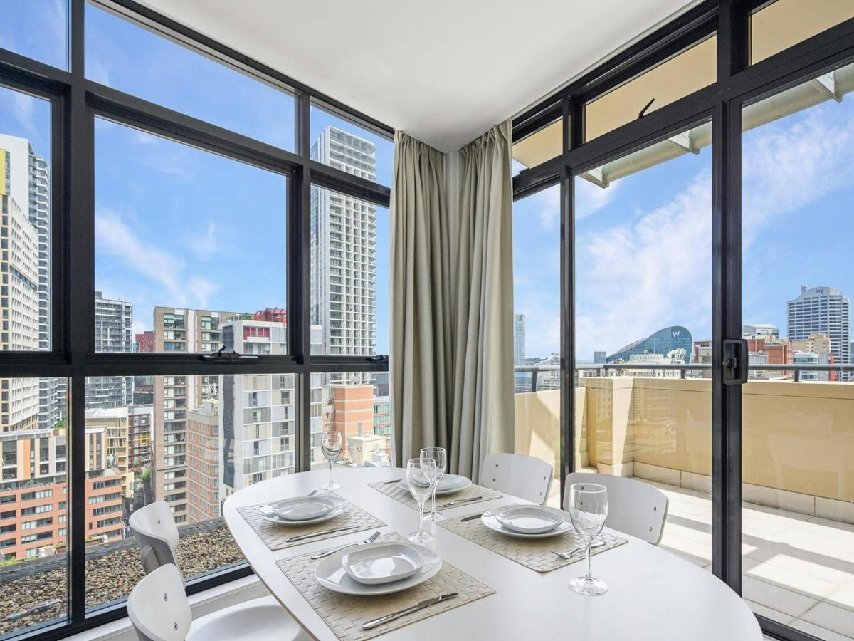 Dining area with table setting and floor-to-ceiling windows leading to the balcony with city views.