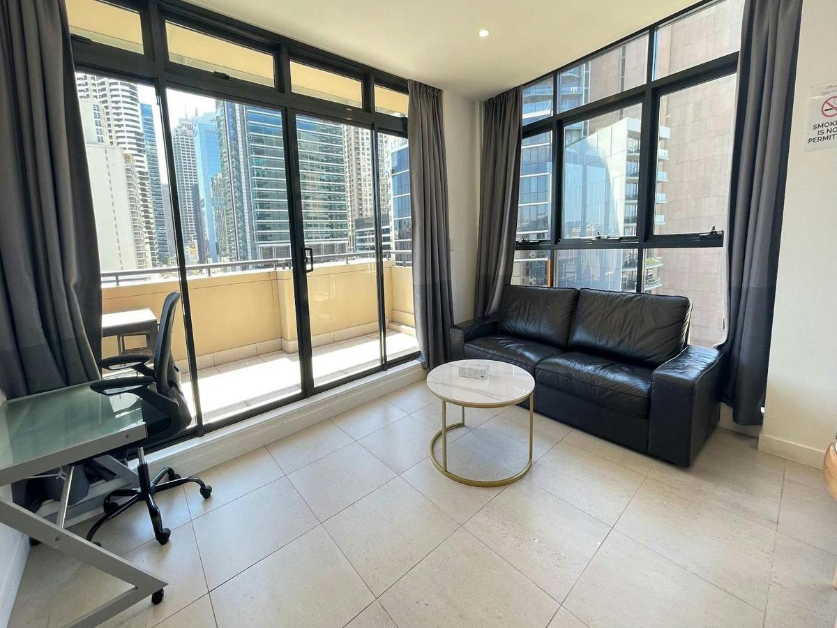 Living room with leather sofa, coffee table, and floor-to-ceiling windows.