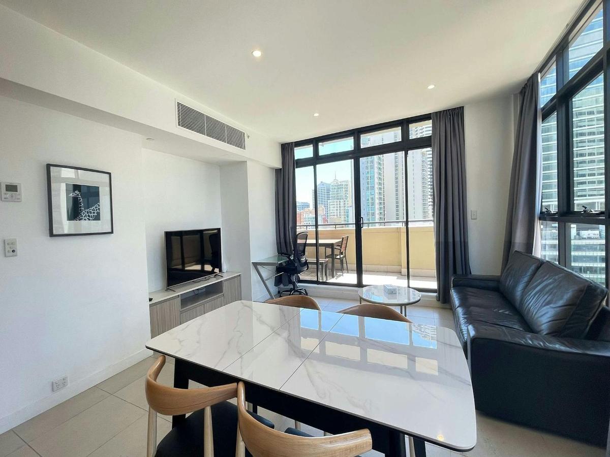 Open-plan living and dining area with sofa seating, TV, dining table, and balcony access.