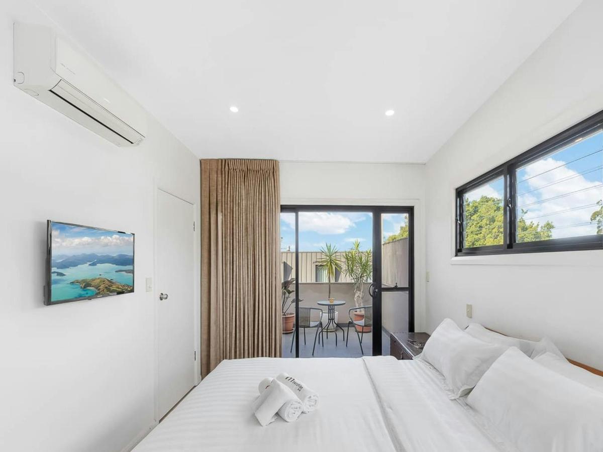 Bright bedroom featuring a comfortable bed and large windows with leafy views.