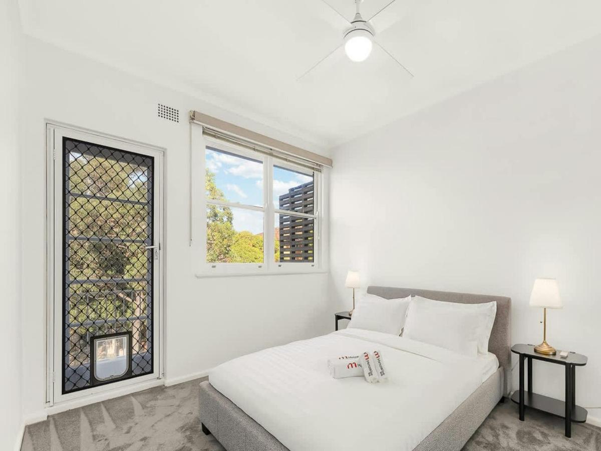 Bright bedroom with queen bed, bedside table, and large windows with natural light.