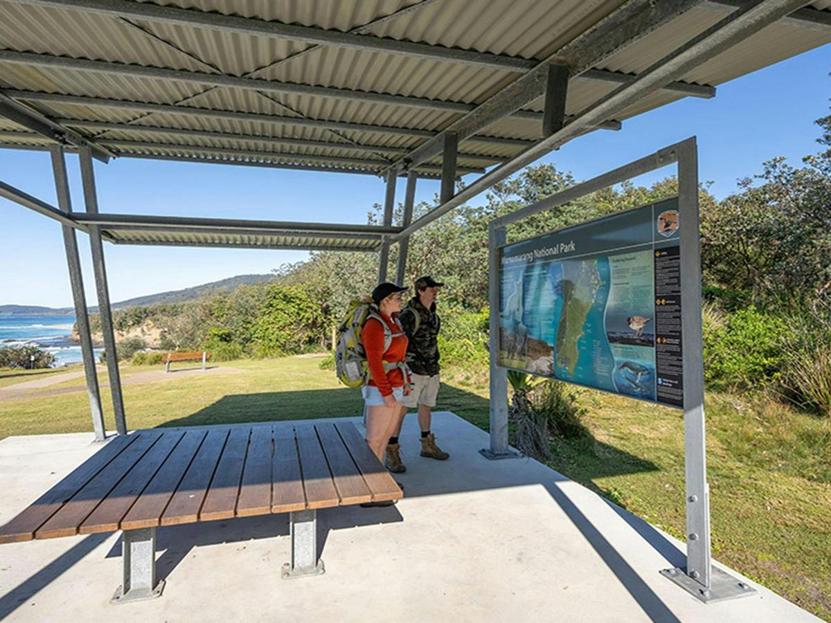 Visitors reading a park sign under shelter at Pretty Beach picnic area. Credit: John Spencer &copy;