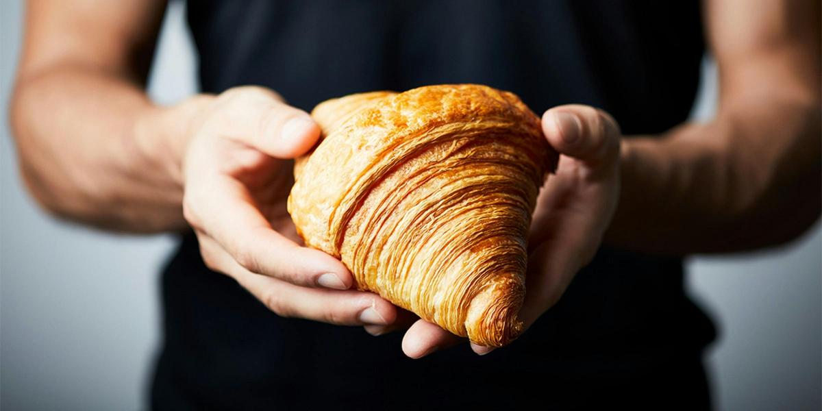 Person wearing black shirt holding a golden croissant