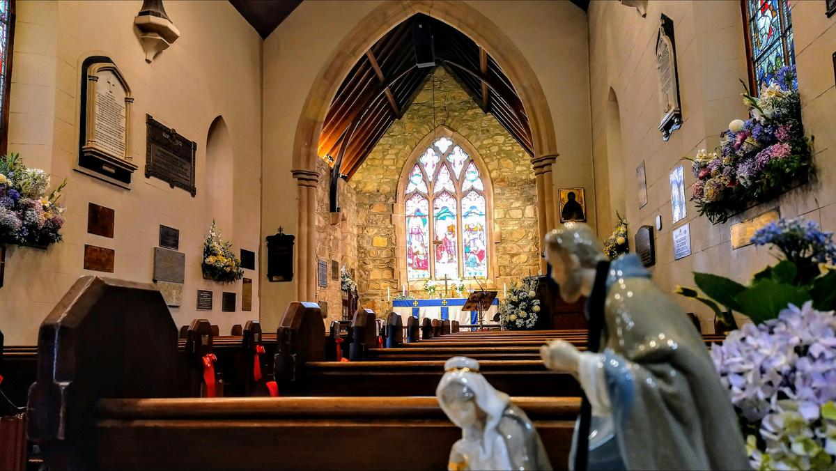 Stained glass window inside stone church with wooden pews and colourful flowers