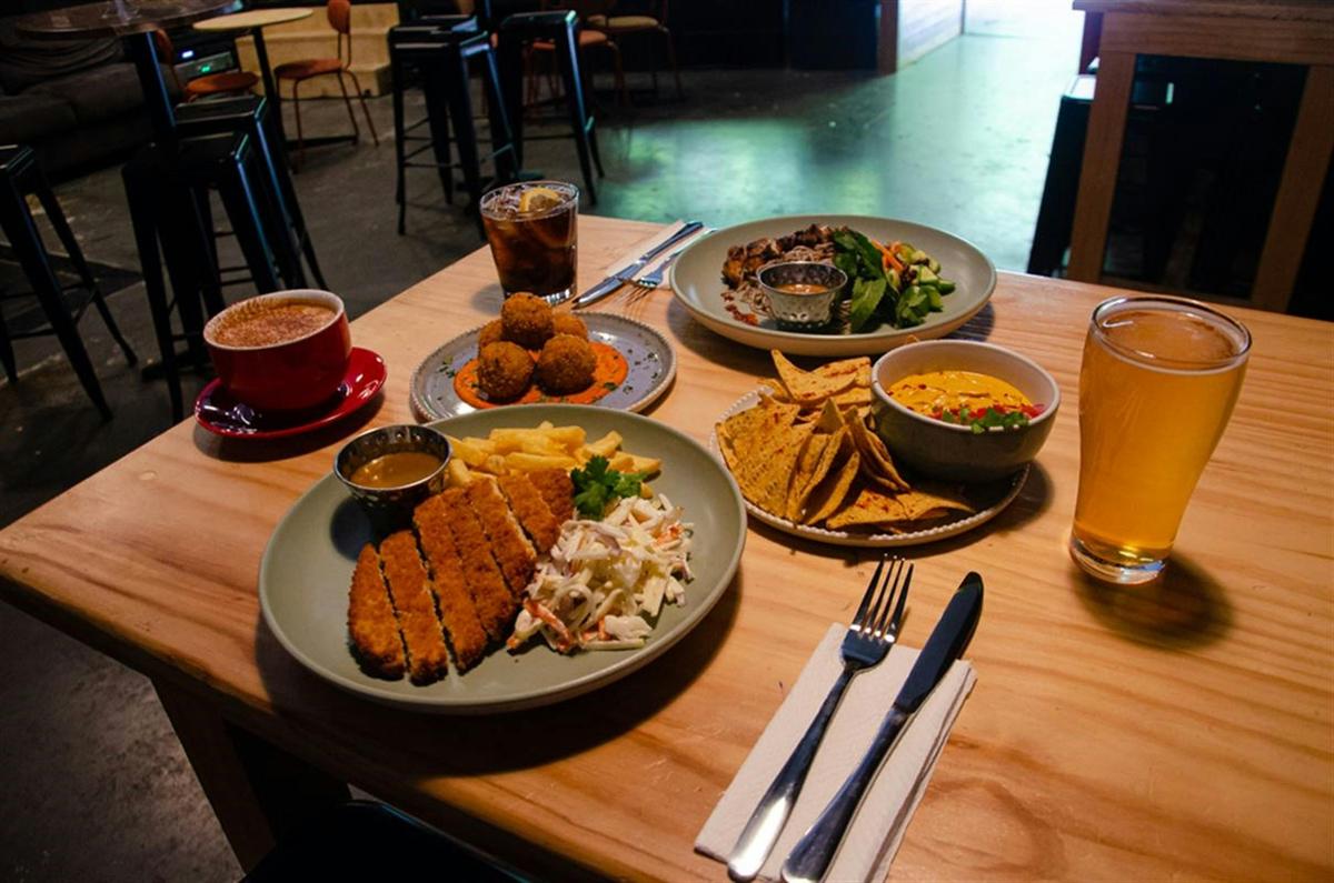 Variety of Dissent's food offerings set out on a wooden table. Arancini, schnitzel and corn chips.