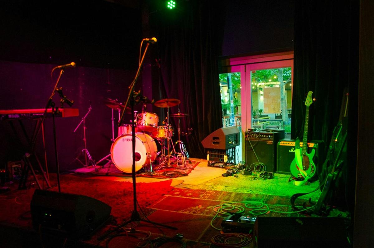 Image of a drumset, microphone, a couple of amps on  a stage with red and green lighting.