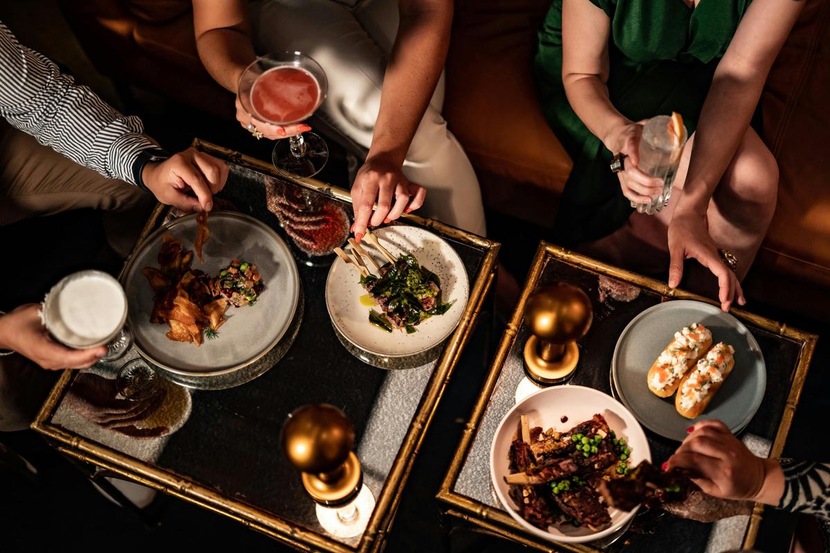 A table with food and cocktails and people eating and drinking with their hands
