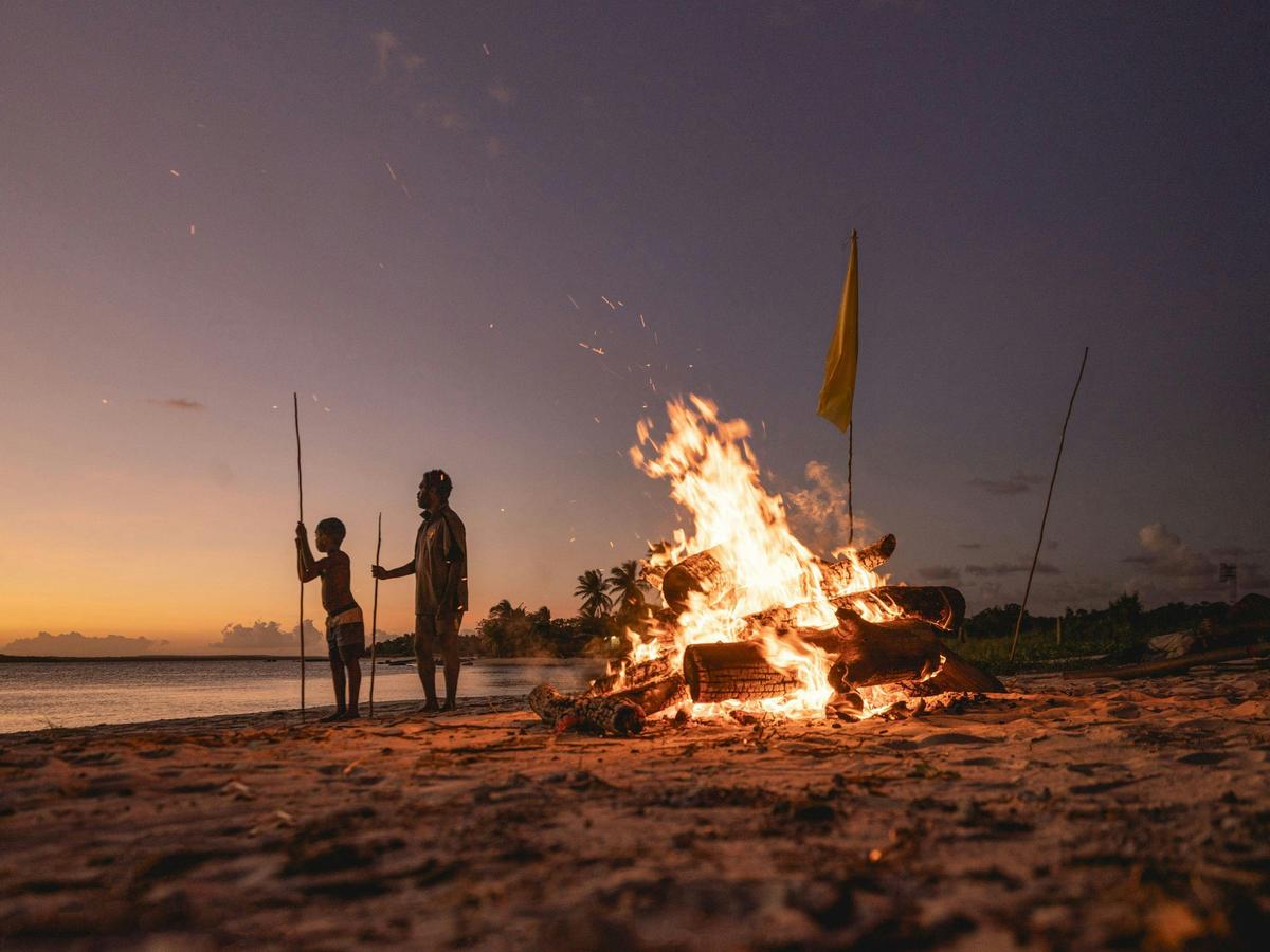 Aboriginal man and child holding spears next to a campfire on the beach in East Arnhem Land