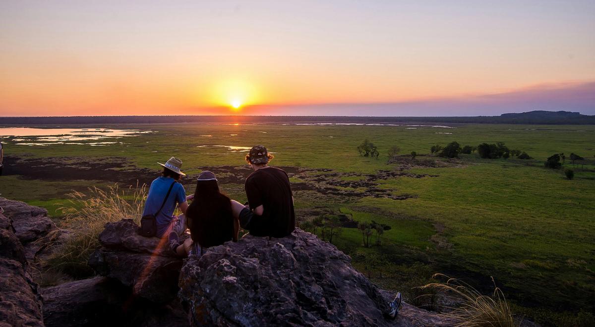Three people sitting on a rock in  Ubirr watching the sunset