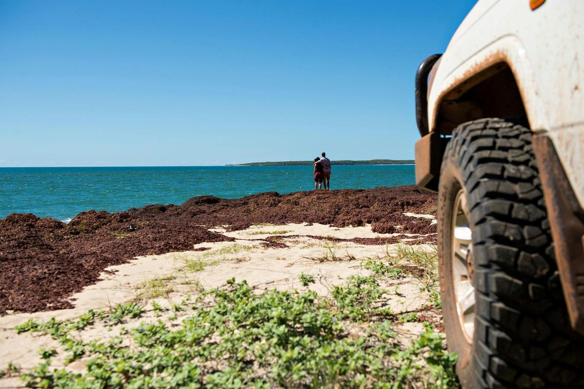 Two people at the beach with car and tyre in foreground