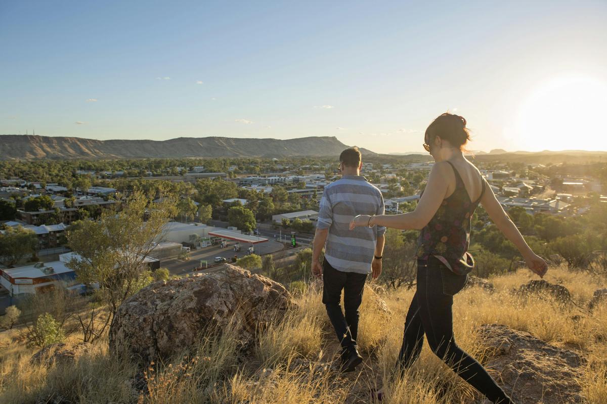 a_couple_walking_on_anzac_hill_overlooking_alice_springs_at_sunset