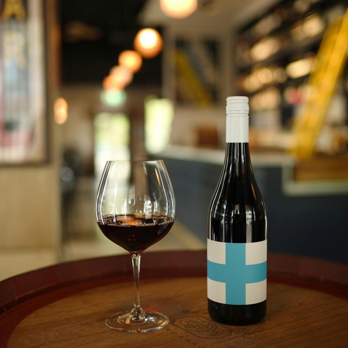 A glass of wine next to it's bottle in a wine barrel