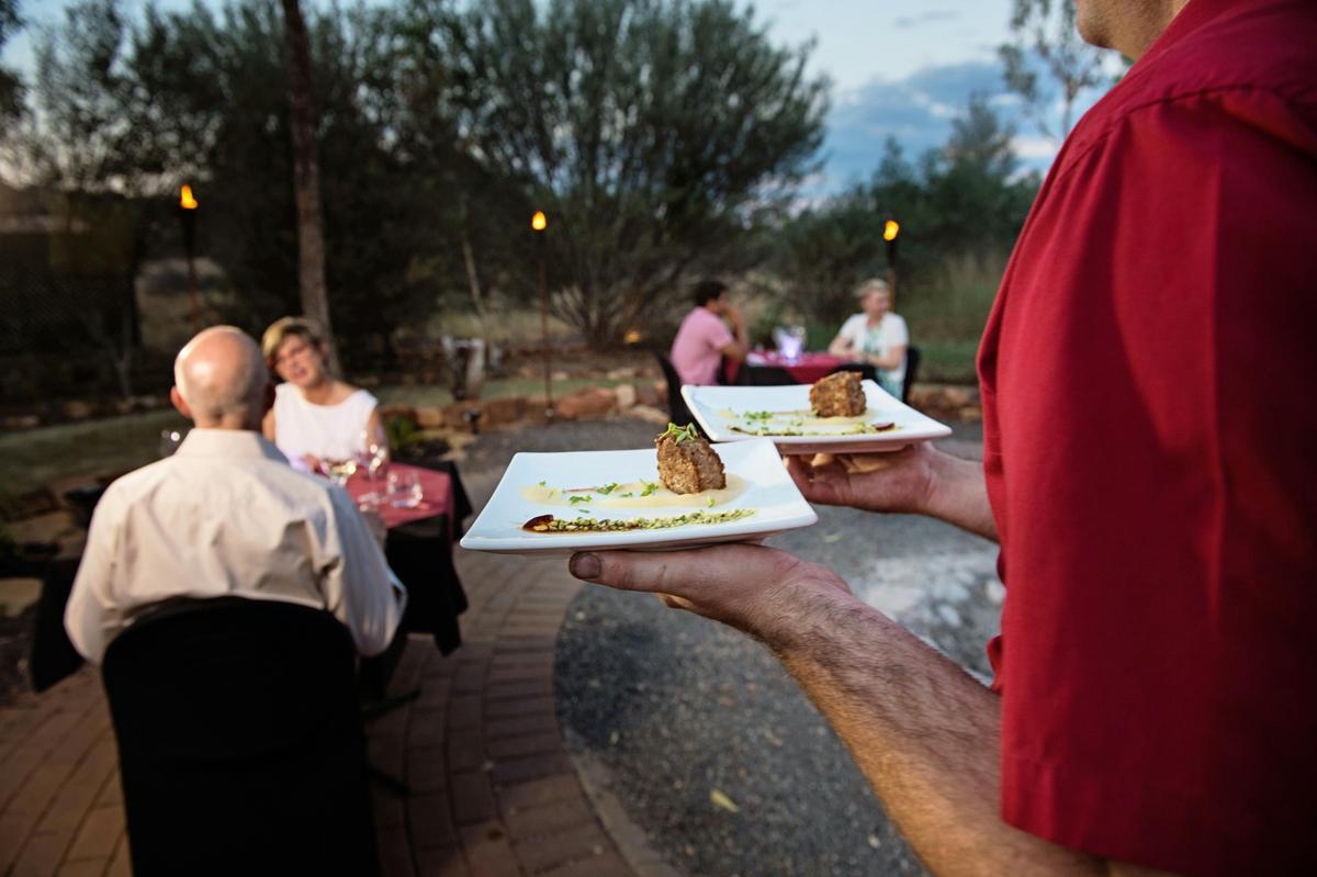 A waiter carrying plates of food at Under a Desert Moon dining experience at Kings Canyon Resort