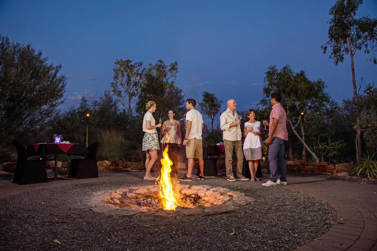 A group of people standing around a fire pit at Under a Desert Moon dining experience