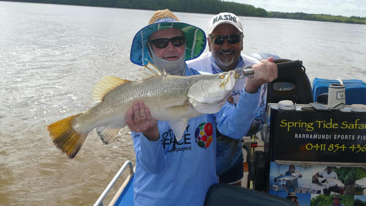 Two men standing in a boat holding a barramundi.