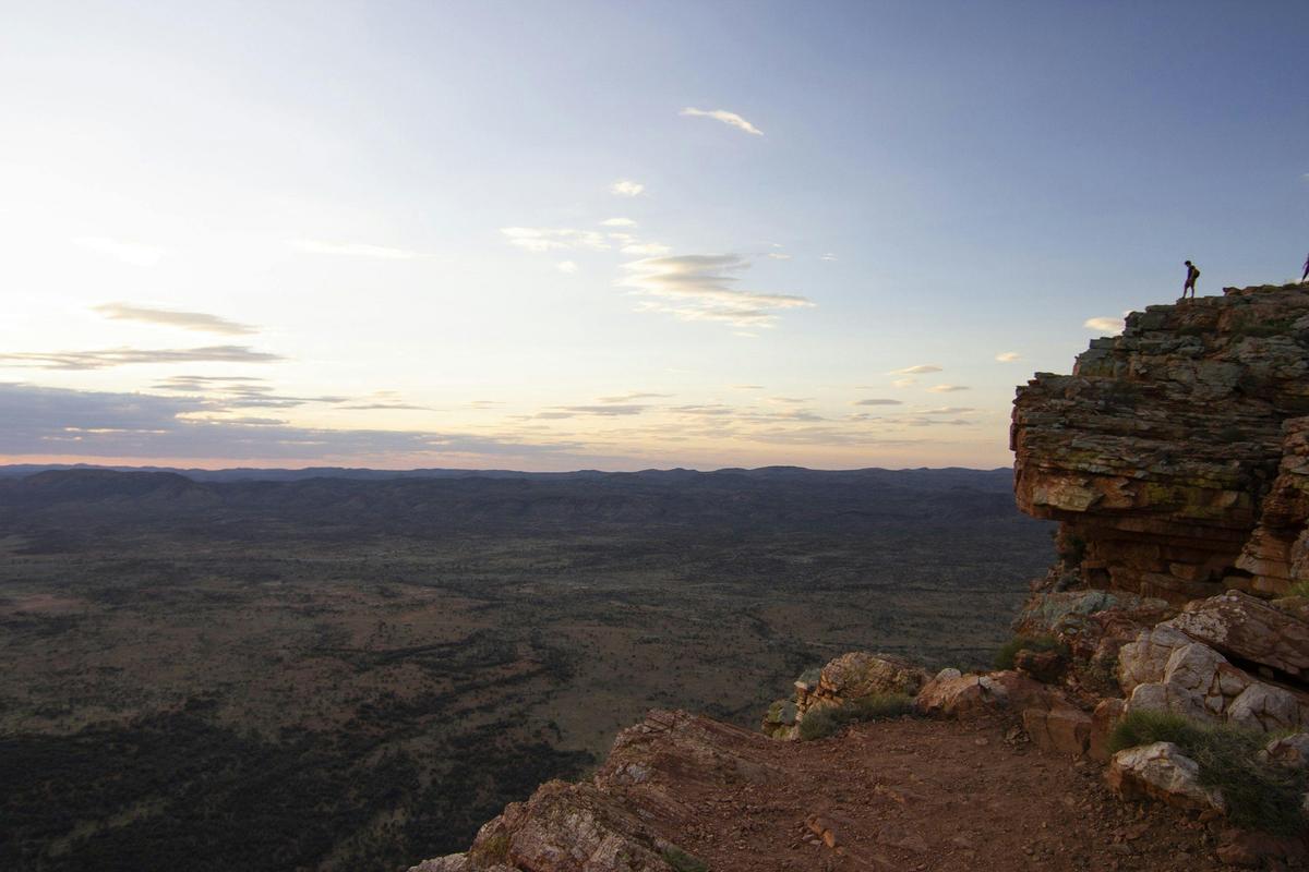 Man up on a rock escarpment looking over West Macdonnell Ranges