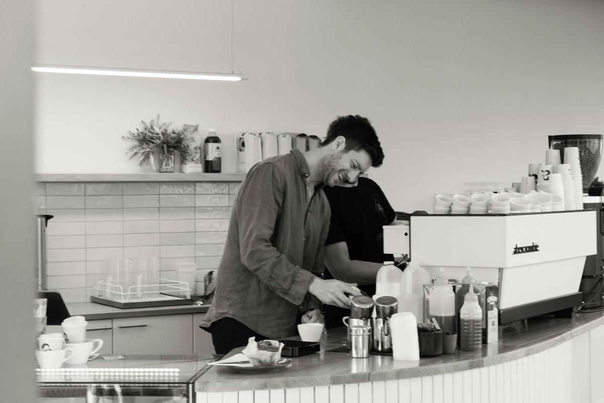 A man smiles as he prepares a coffee behind the counter of Abercrombie Coffee.