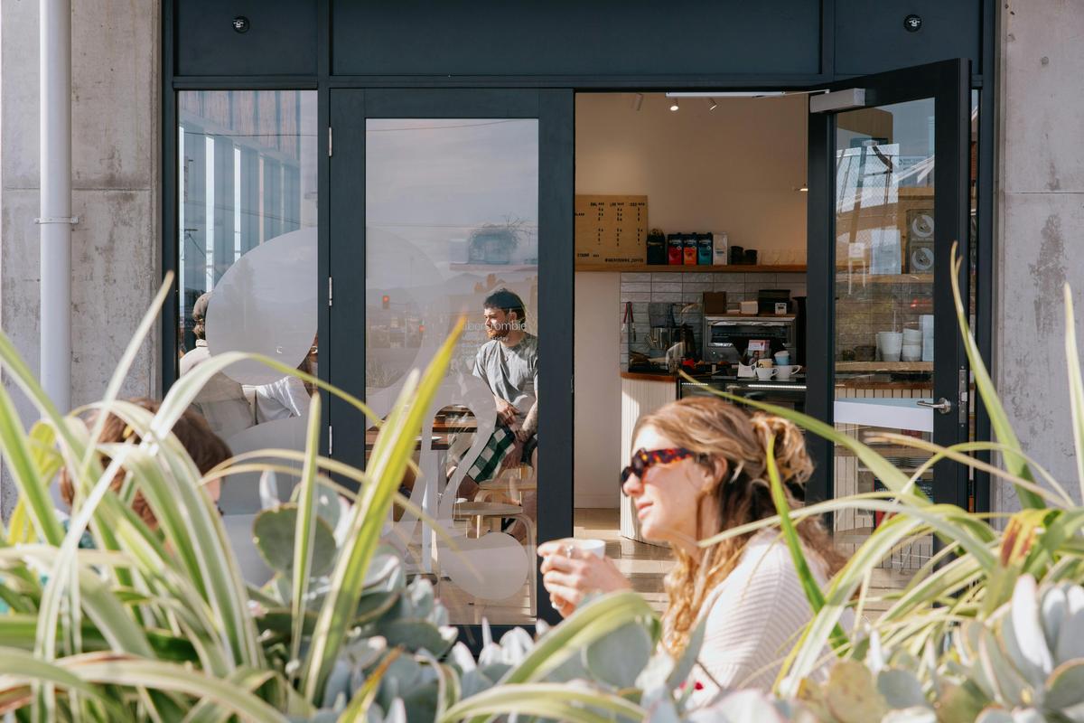 Woman sits outside cafe holding a coffee cup with sunglasses on.