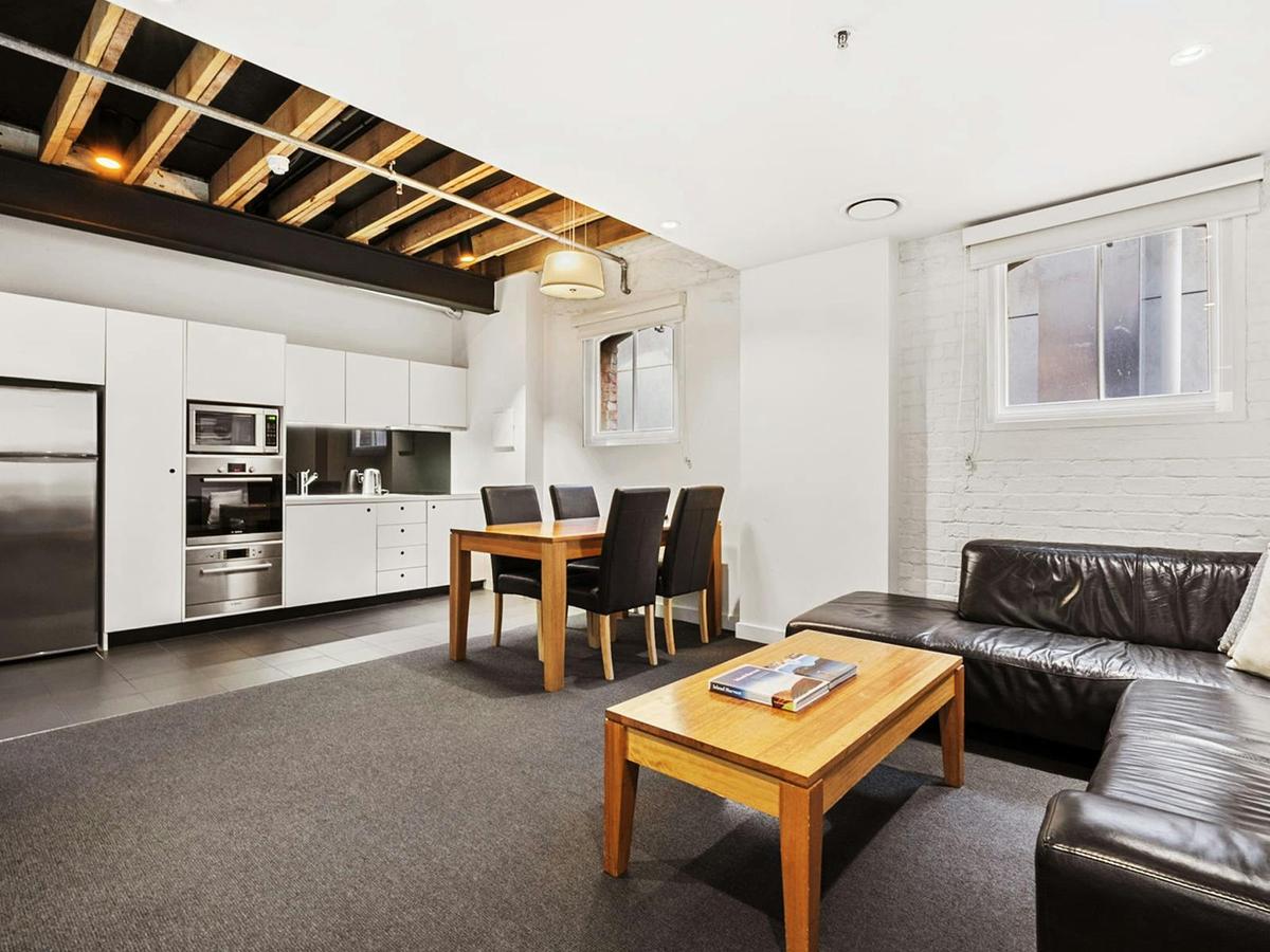 White kitchen and lounge with leather sofas under exposed timber ceiling beams.