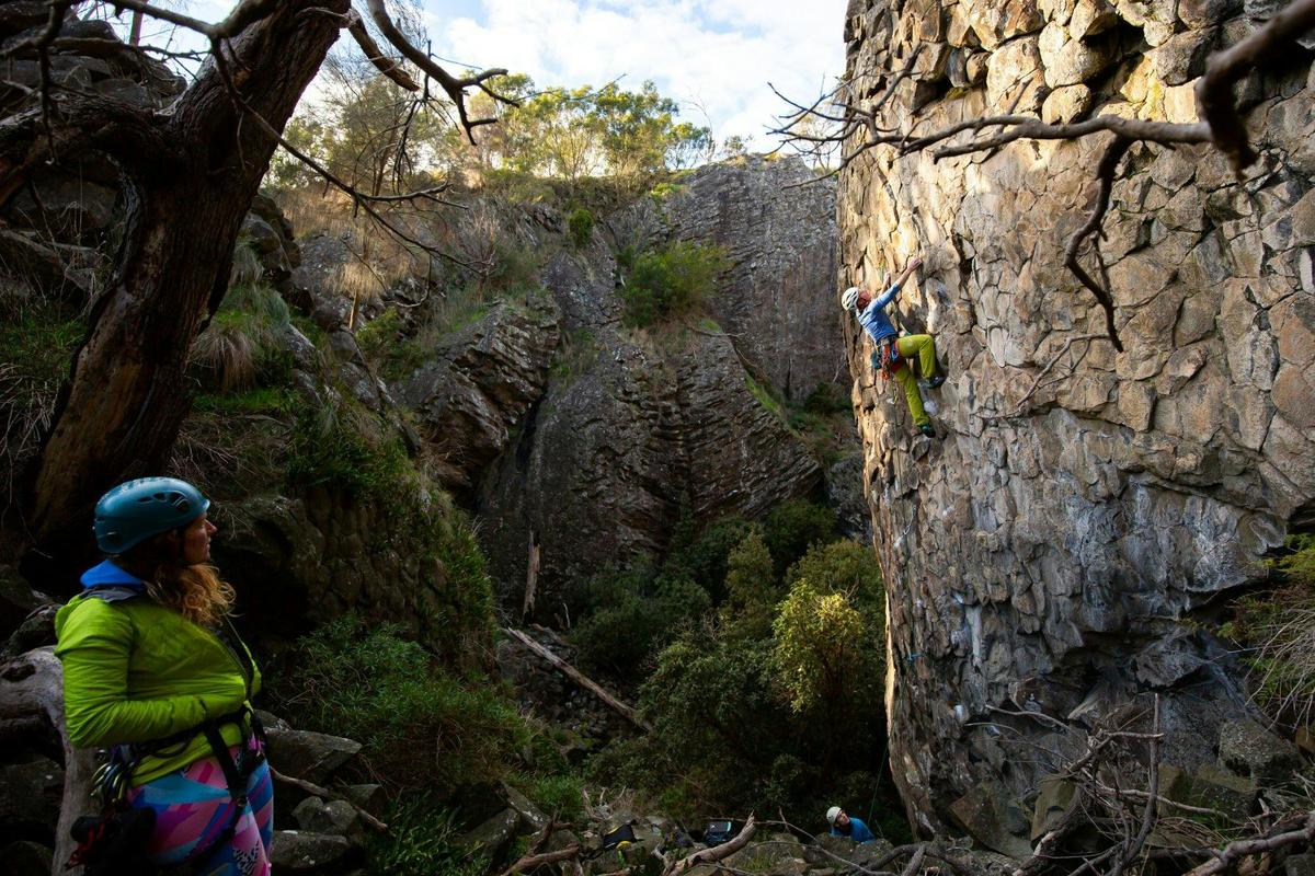 A climber watches another climb on a vertical rock.