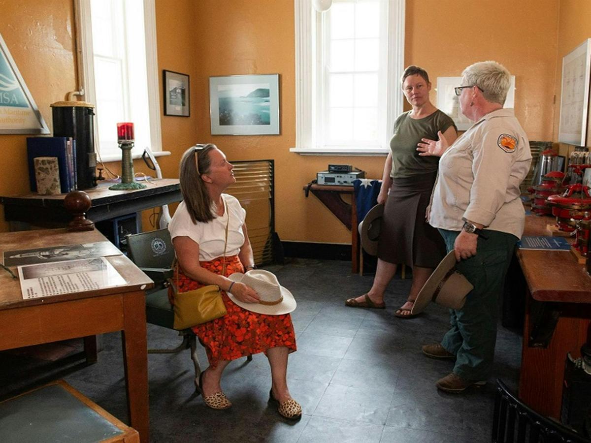 Two visitors listen to a tour guide in the lighthouse keeper's office, Smoky Cape Lighthouse, Hat