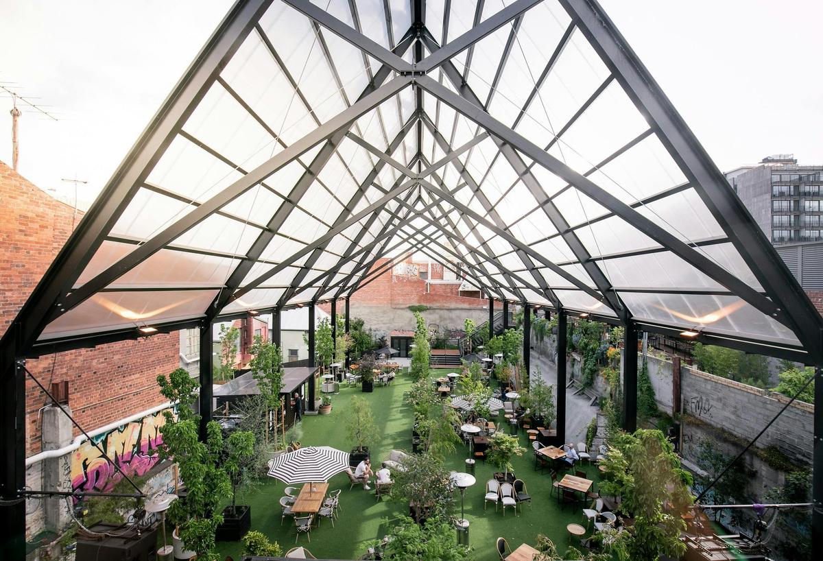 The 18 metre tall Cathedral black frame shelters the lawn space with tables and plants beneath