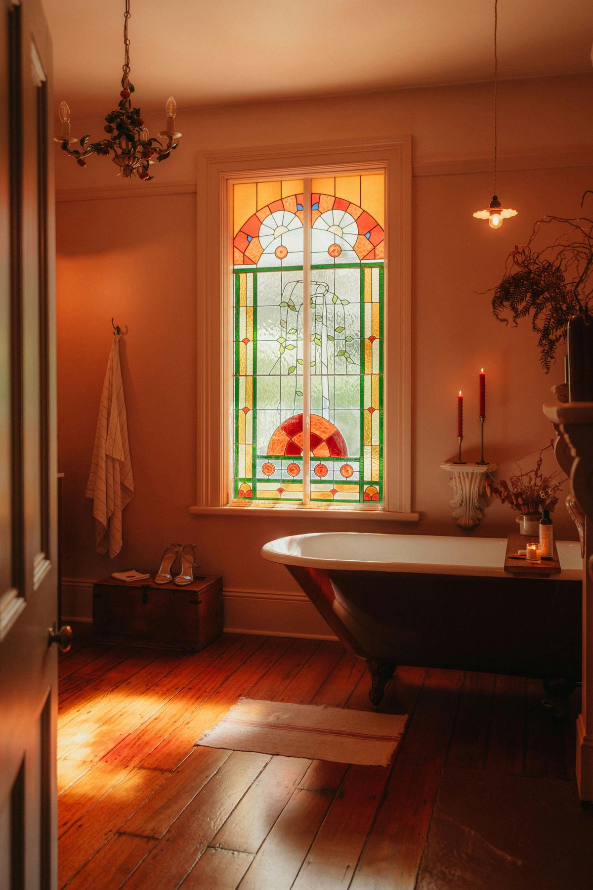 A clawfoot bath beneath stained glass - colour, light, and quiet retreat.