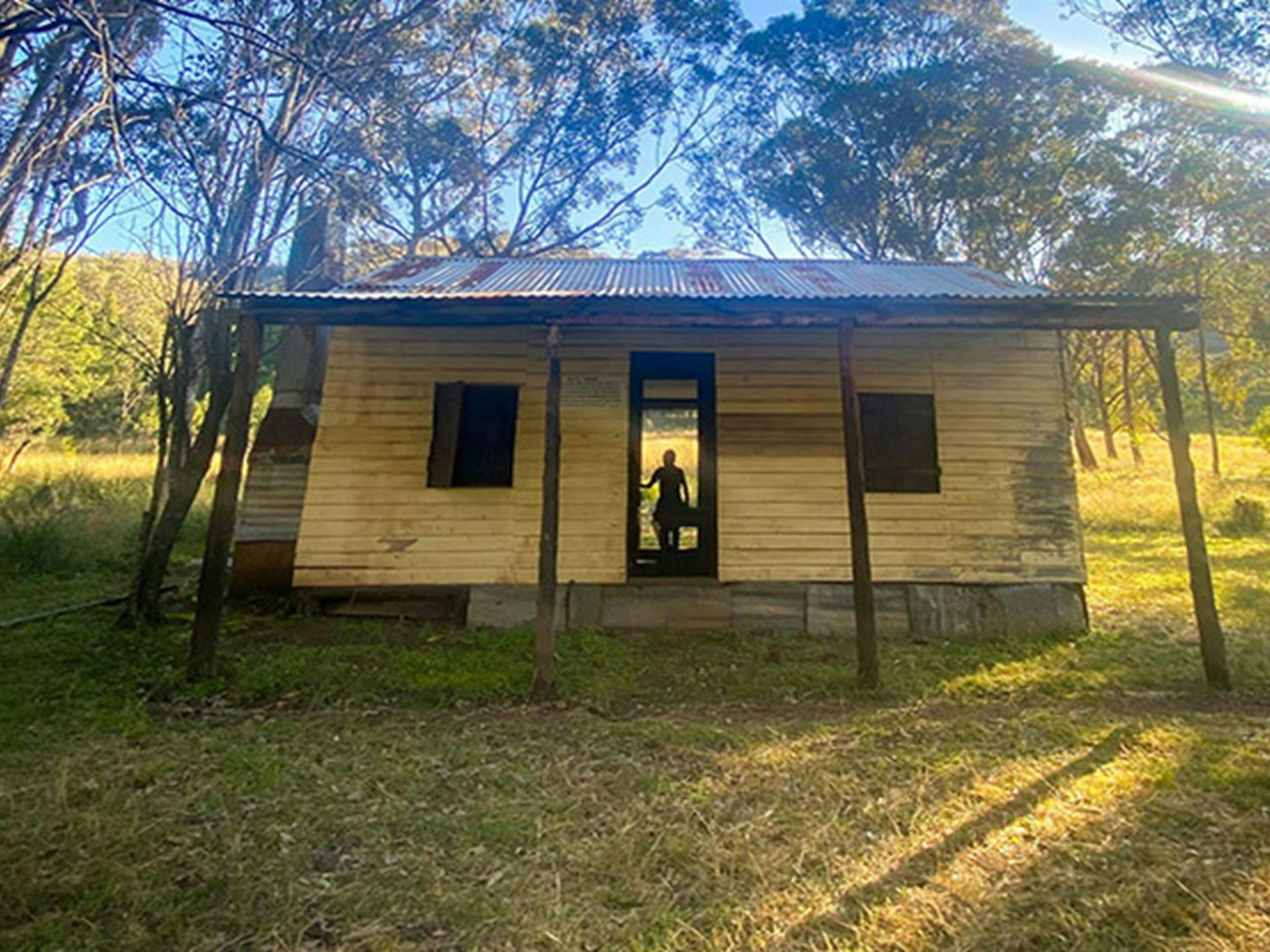 Silhouette of a person in the doorway of Scutts Hut, set in a grassy clearing in open woodland of
