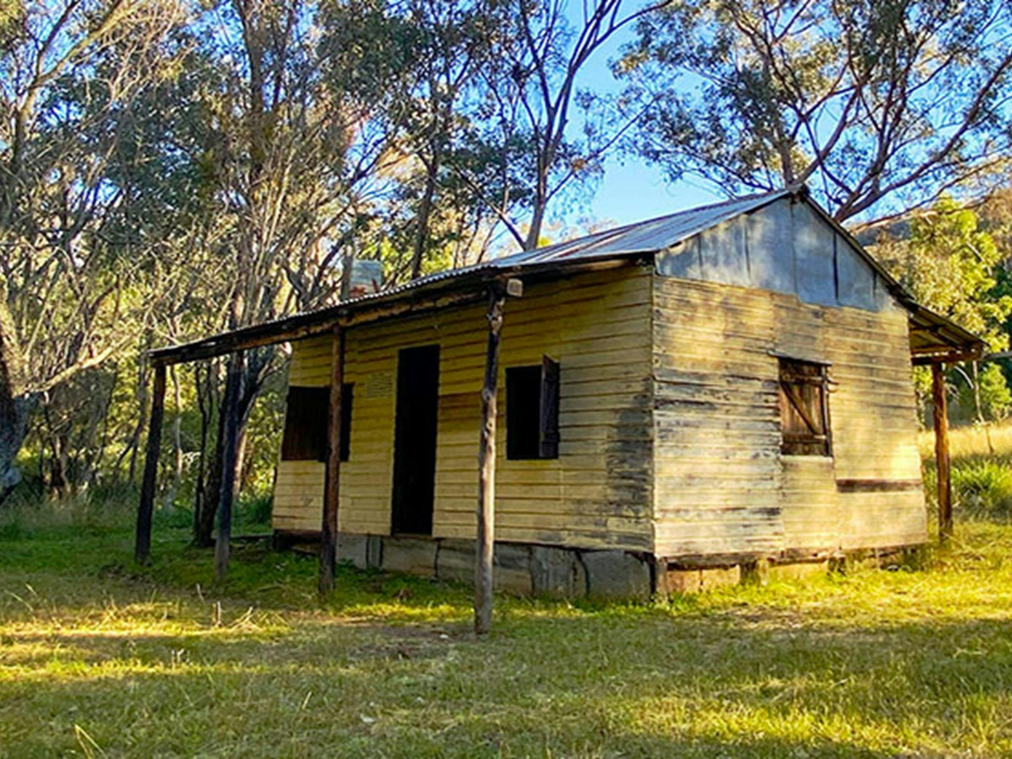 Side view of Scutts Hut set in grassy clearing with hills and bush land in the background. Photo