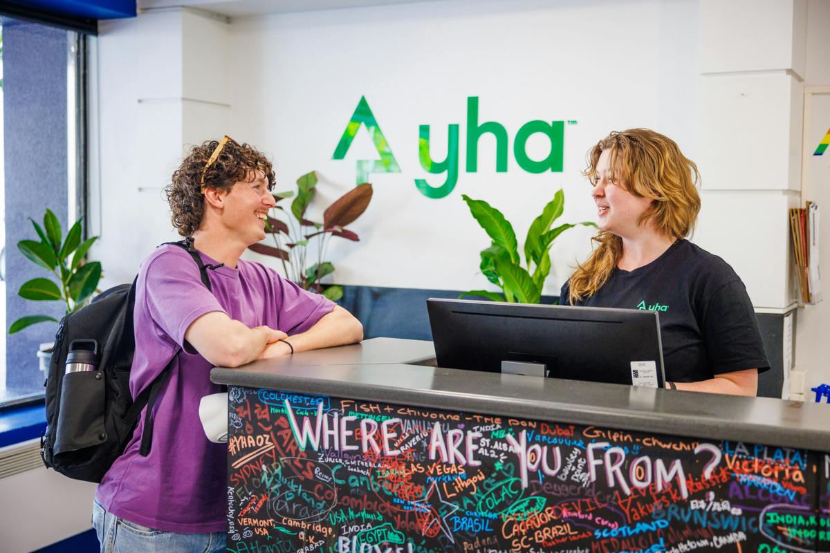 Young man laughing and talking with staff member at reception desk if YHA Hobart Central
