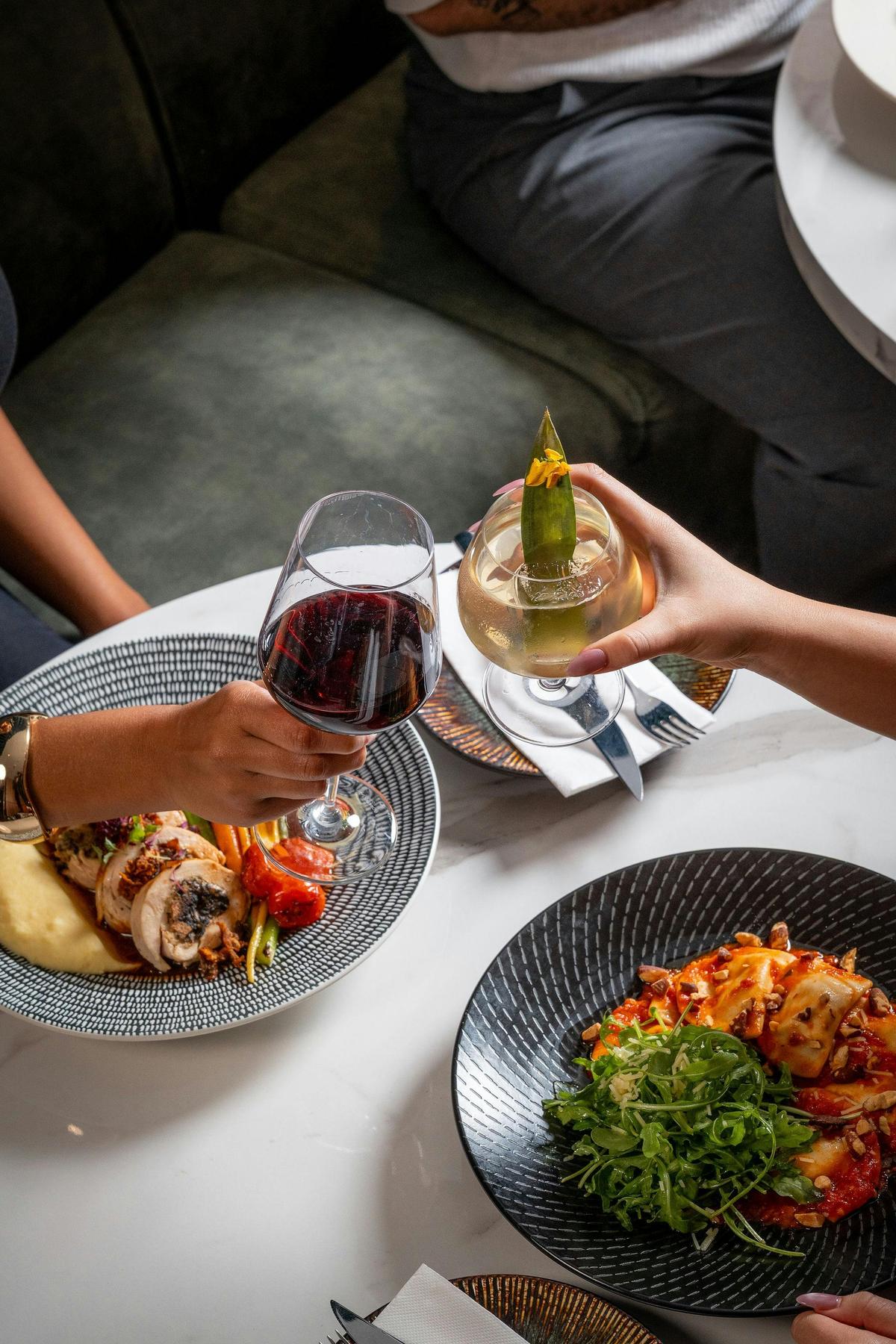 people cheers-ing cocktail and wine over a table of food