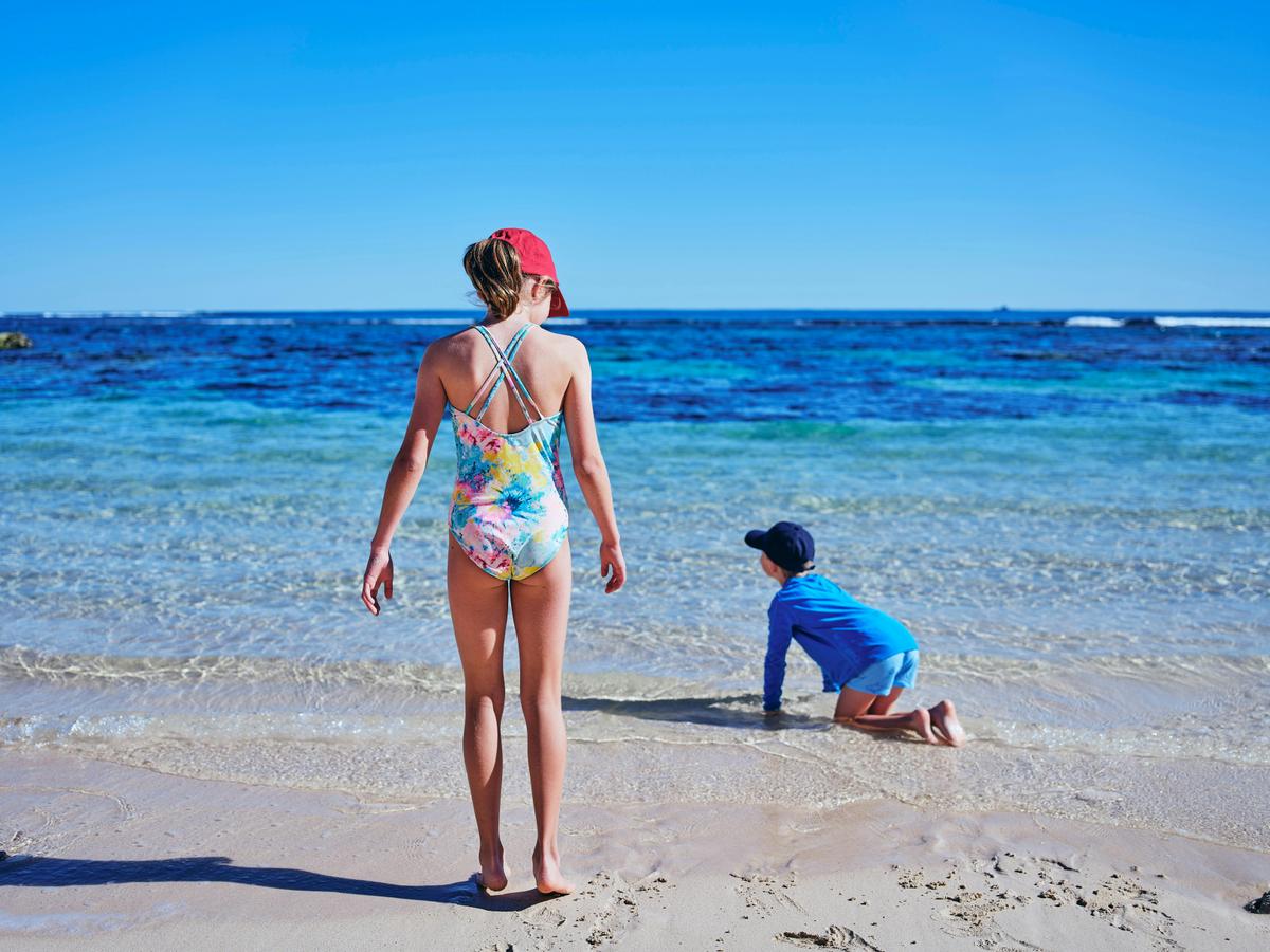 Two kids playing at water's edge on a beach.