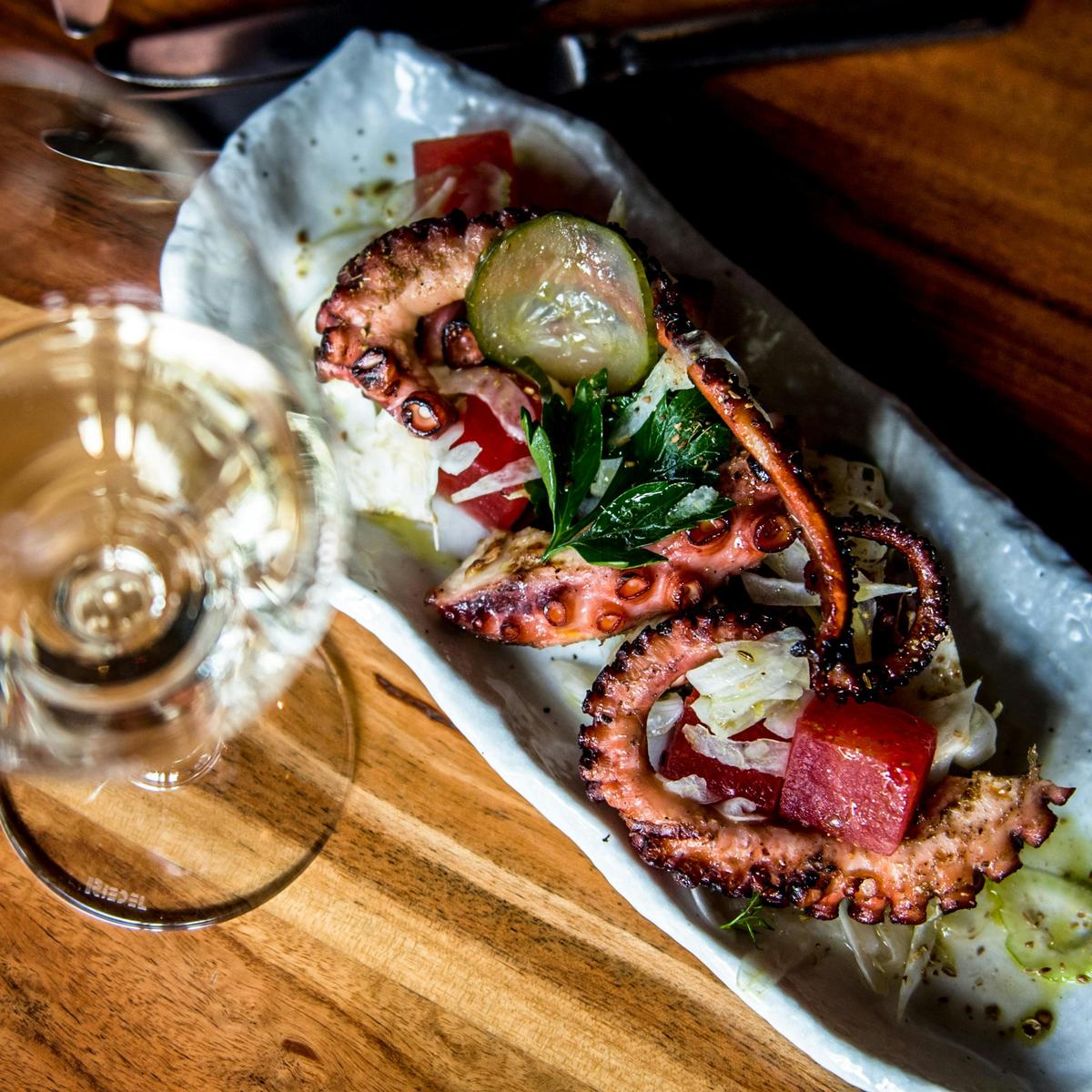 Plated up twice cooked octopus with a glass of white wine taken from above