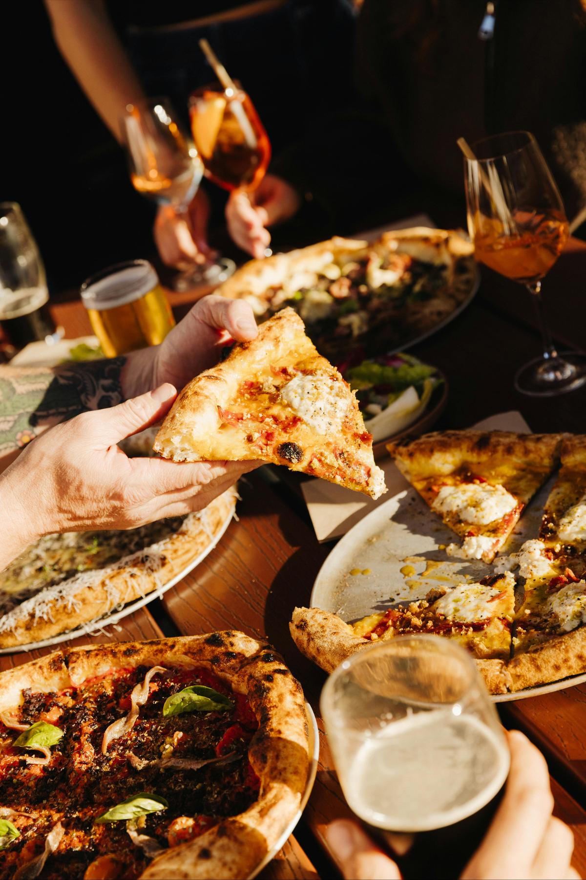 Hand grabbing a slice of pizza from a shared table spread at Found Subiaco.