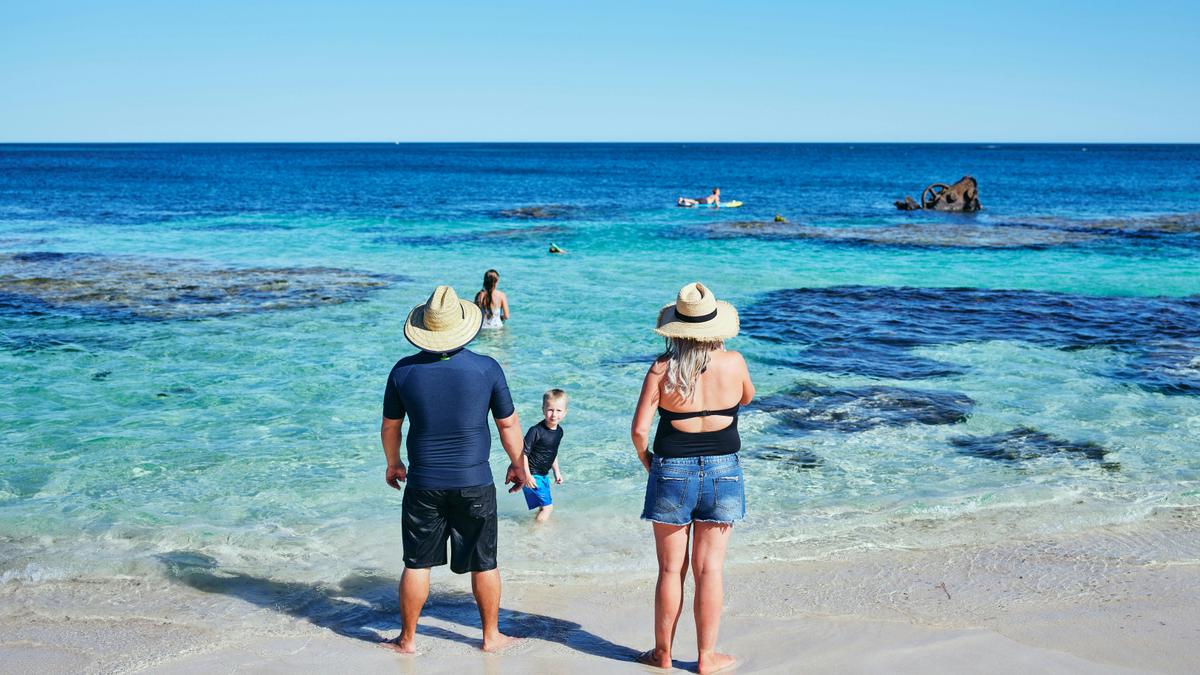 Family standing at water's edge on a sunny beach.