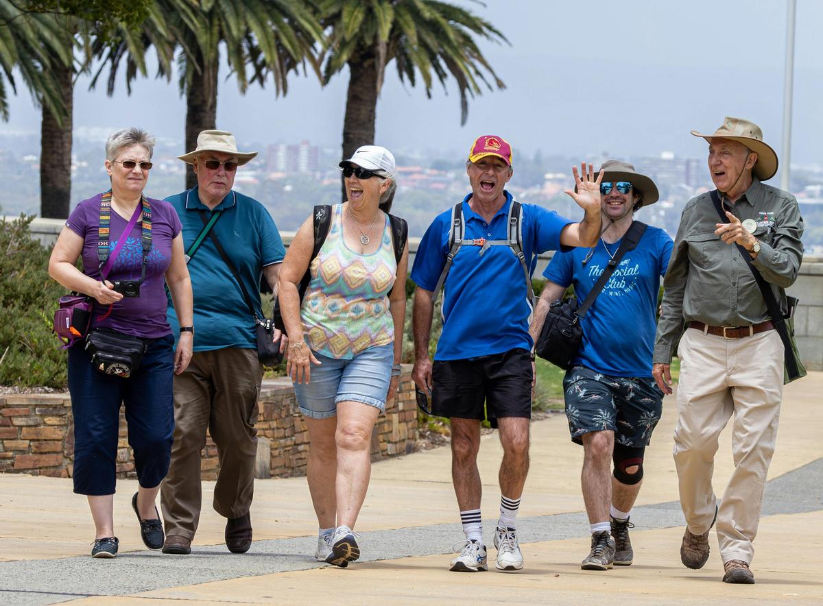 A group of smiling and waving visitors walking with a uniformed Guide