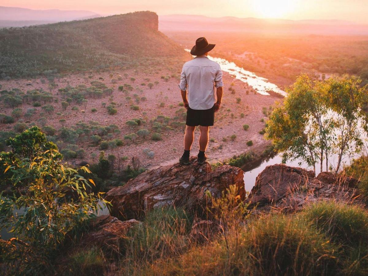 Hiker on a cliff at sunset, overlooking a winding river and vast Australian outback.