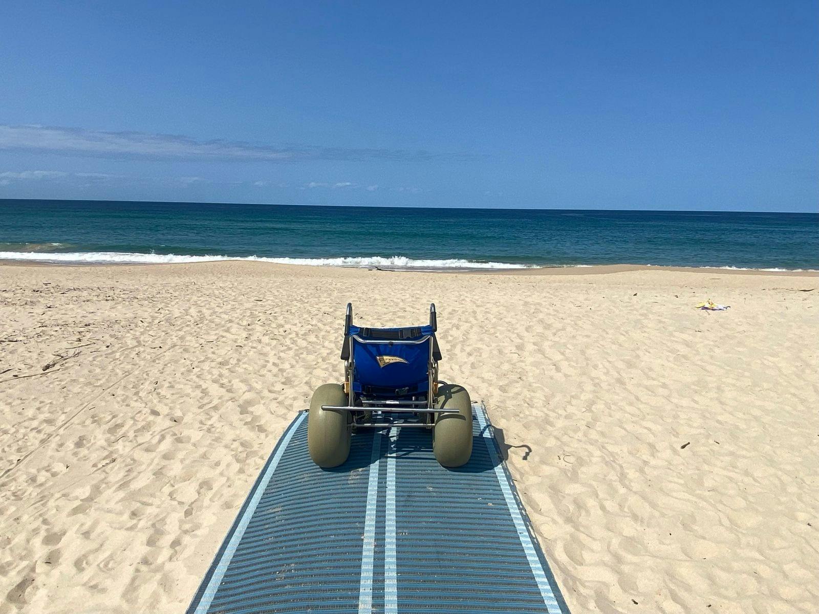 Sand Wheel Chair sitting on a sand matt on the beach with ocean in the distance