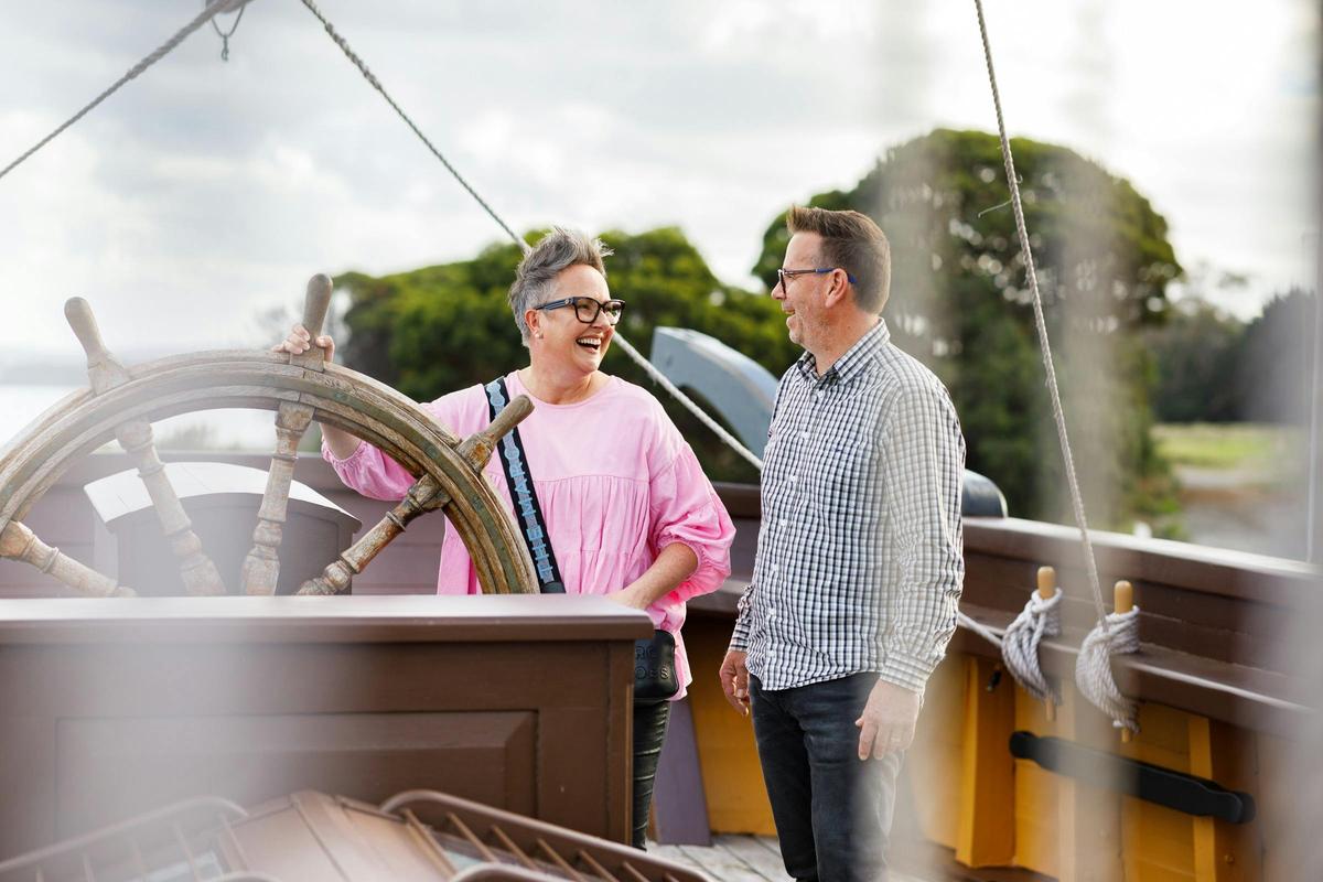 two people on deck of a replica ship near a steering wheel