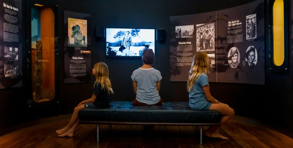 a group of children sit on a large seat looking all directions around at multi media displays