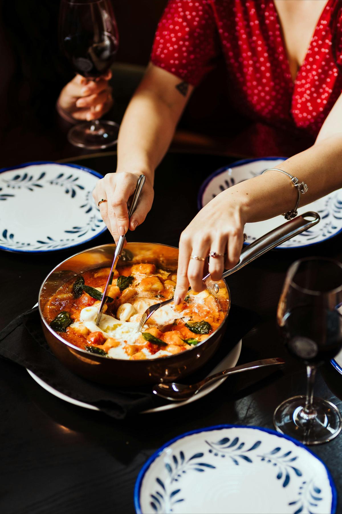 A diner serves gnocchi in a tomato sauce with burrata and basil from a copper pan
