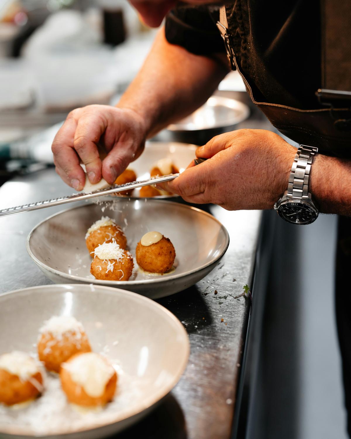 Chef grating cheese over a plate of arancini.