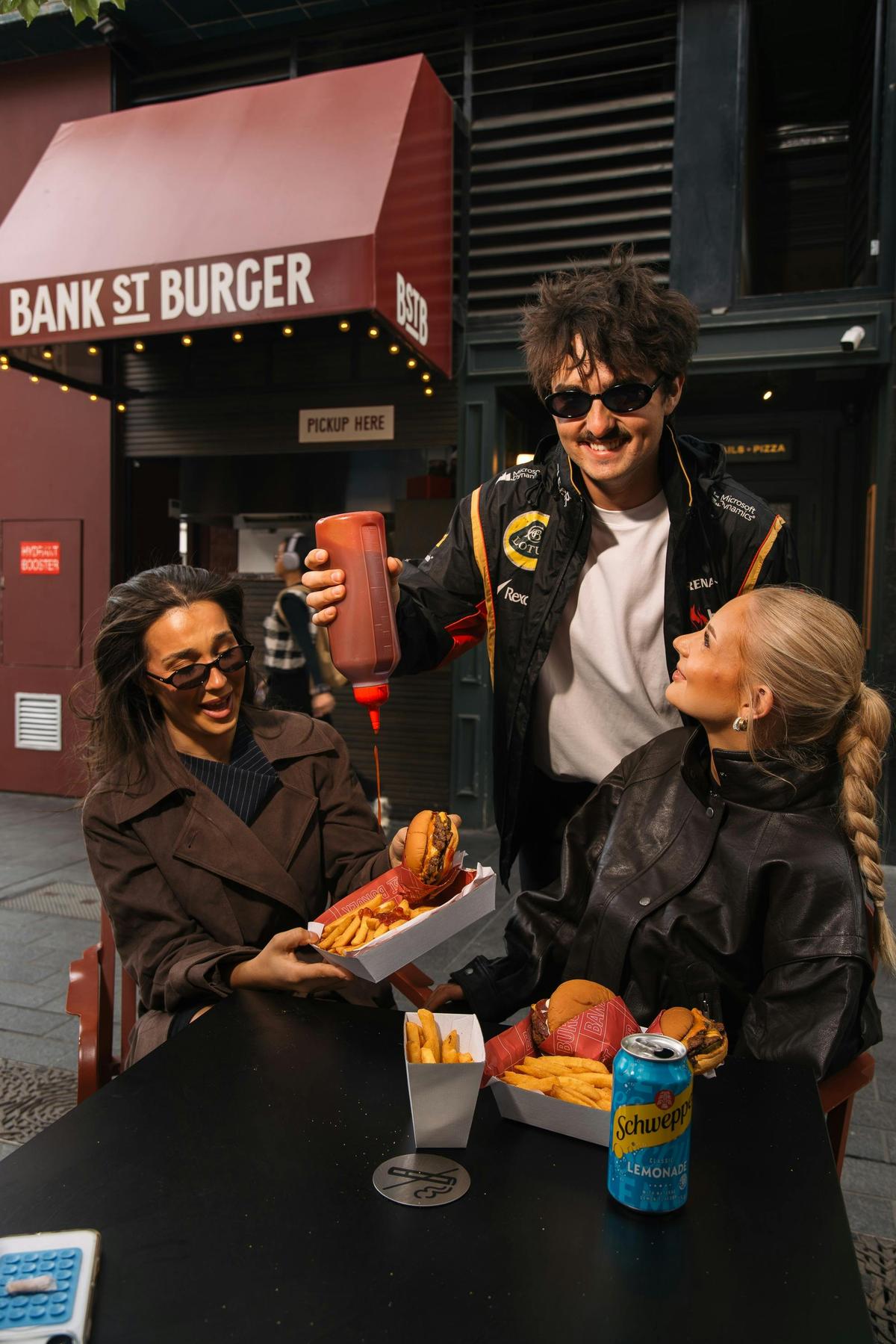 A man pours tomato sauce on some fries as two girls laugh at Bank Street Social