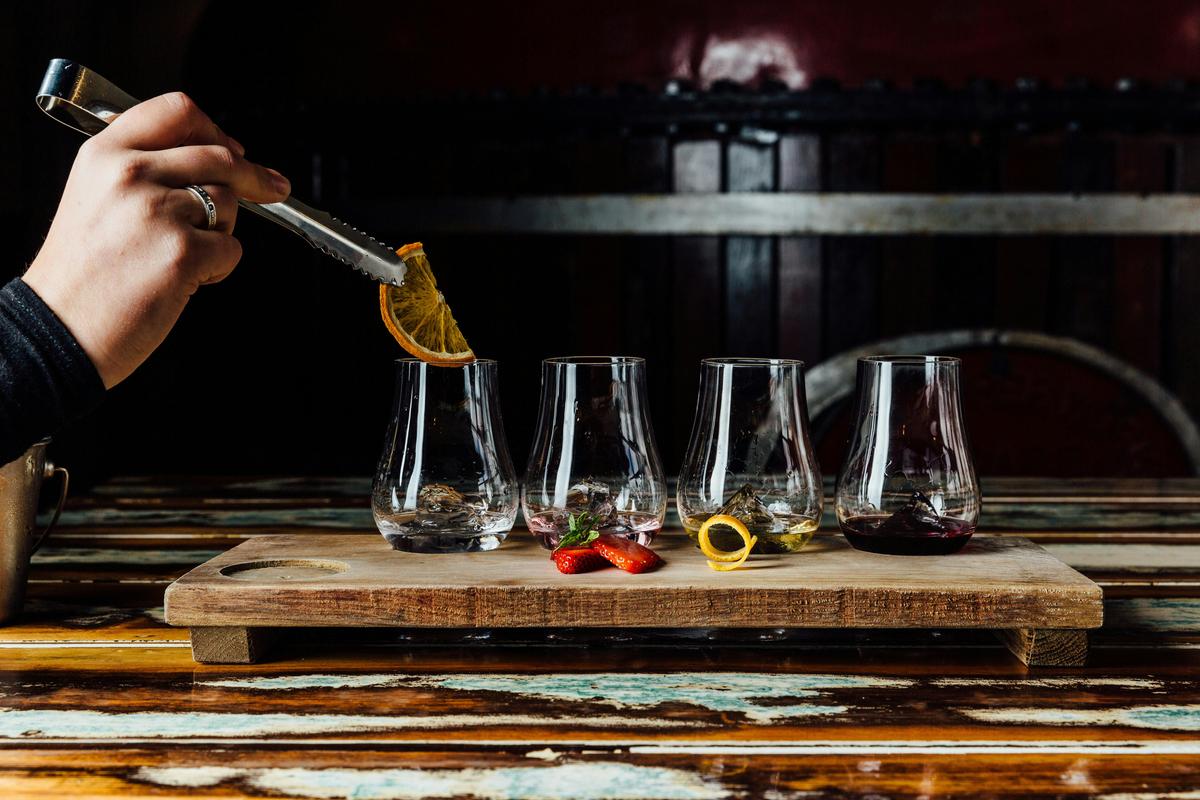 Gin tasting paddle with someone placing a garnish into one of the glasses.