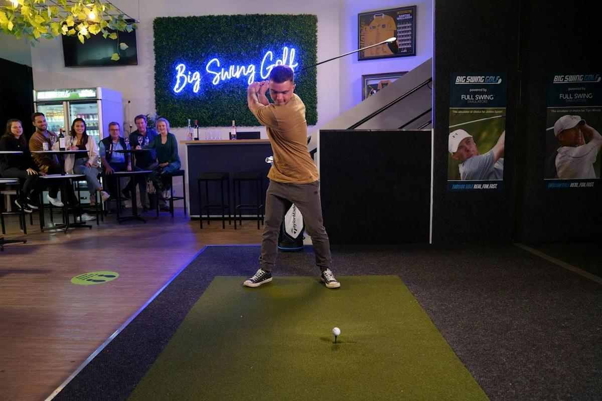 a photo of a man  hitting a ball in a big swing simulator, he ios in the middle of his backswing....
