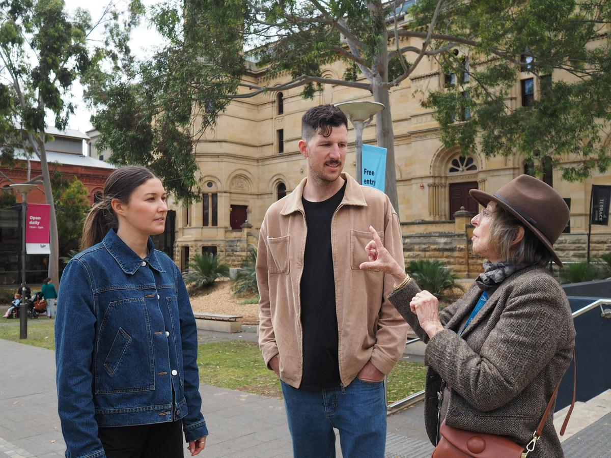 A guide is talking to two people outside the South Australian Museum