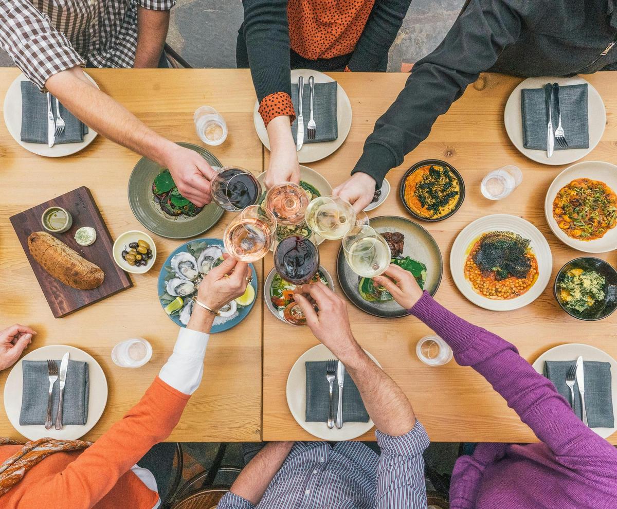 A table filled with food, wine glasses overhead cheers-ing.